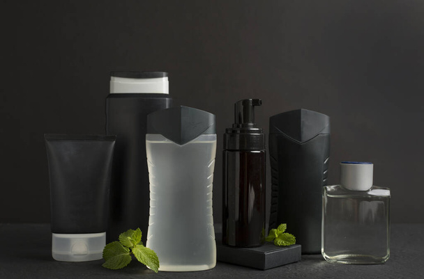 Botellas cosméticas para hombre con hojas de menta sobre fondo negro - Foto, Imagen