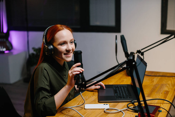 Dziewczyna prezenter radia przemawia do mikrofonu podczas transmisji w stacji radiowej. Online blogger podczas strumienia. - Zdjęcie, obraz