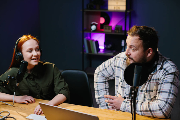 two radio hosts in headphones laughing while recording podcast in studio togethe - Valokuva, kuva
