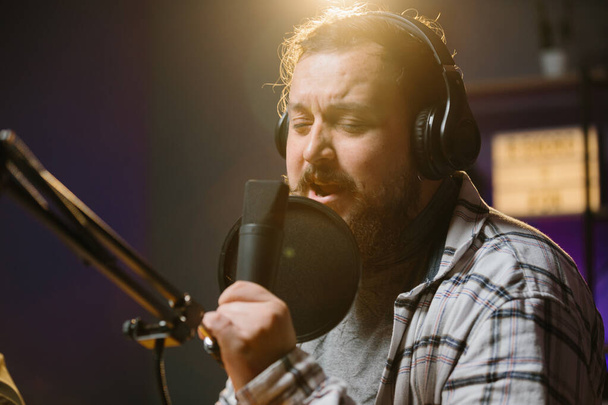 Portré egy rádiós műsorvezetőről vagy bloggerről egy otthoni stúdióban. Egy fejhallgatós férfi kifejezetten a mikrofonba beszél.. - Fotó, kép