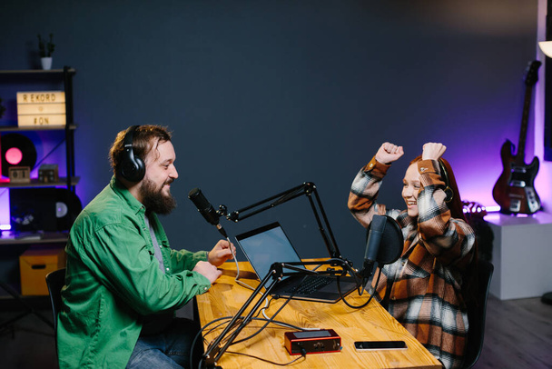 A podcast host and a guest have fun chatting during a live online broadcast in a home studio. - Фото, изображение