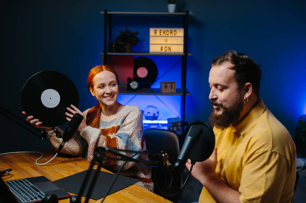 Müzik blogcuları podcast 'lerinin yeni bir bölümünü kaydediyor. Bir adam ve bir kadın stüdyoda müzik hakkında konuşuyorlar, kadın elinde plakla geziyor.. - Fotoğraf, Görsel