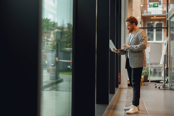 Przystojny przedsiębiorca pracujący na laptopie stojącym we współczesnym współpracowniku w ciągu dnia pracy - Zdjęcie, obraz