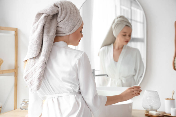 Νεαρή γυναίκα με κρέμα μετά το ντους κοντά στον καθρέφτη στο μπάνιο - Φωτογραφία, εικόνα