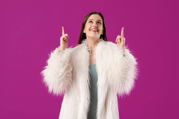 Young woman in fur coat pointing at something on purple background - Photo, Image
