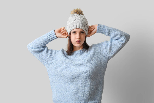 Mujer joven disgustada en ropa de invierno sobre fondo claro - Foto, imagen