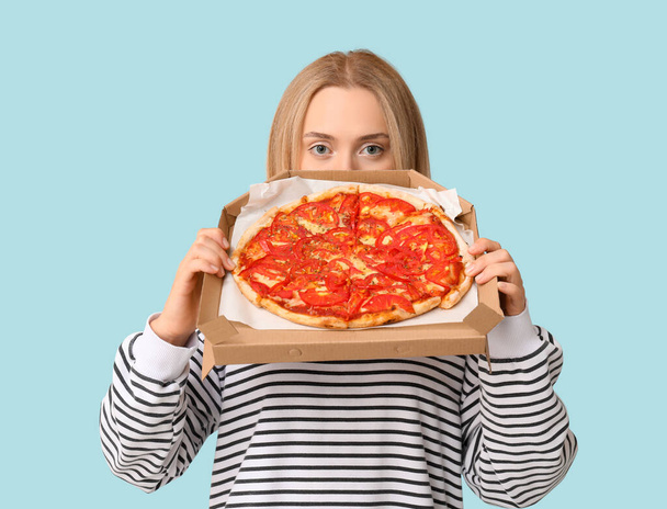 Elinde mavi arka planda lezzetli pizzayla karton kutu tutan genç bir kadın. - Fotoğraf, Görsel