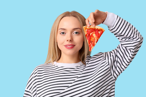 Jeune femme tenant morceau de pizza savoureuse sur fond bleu - Photo, image