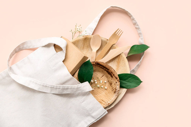 Текстильна сумка з одноразовим екологічним посудом та листям на рожевому фоні - Фото, зображення