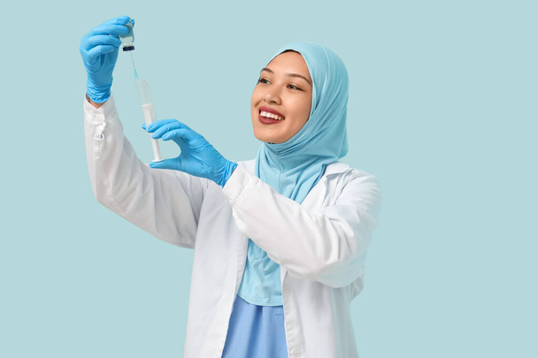 Жінка-мусульманин у хіджабі з ампулом та шприцом на синьому фоні. концепція Всесвітнього дня хіджабу - Фото, зображення