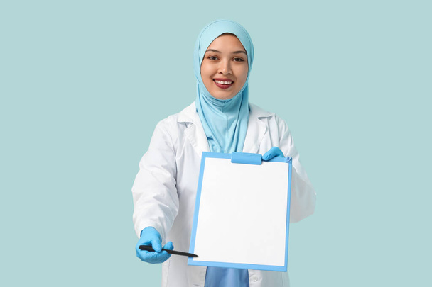 Doctora musulmana en hiyab con portapapeles sobre fondo azul. Concepto del Día Mundial del Hijab - Foto, imagen