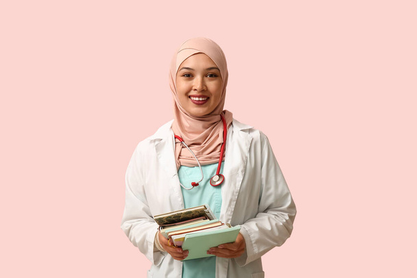 Γυναίκα Μουσουλμάνα γιατρός με μαντίλα και ημερολόγια σε ροζ φόντο. Παγκόσμια ημέρα χιτζάμπ έννοια - Φωτογραφία, εικόνα