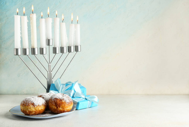 Menorah avec des bougies brûlantes, des beignets et des cadeaux pour la célébration de Hanoukka sur fond de lumière - Photo, image