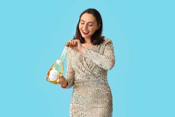 Beautiful young woman with champagne bottle on blue background - Photo, Image