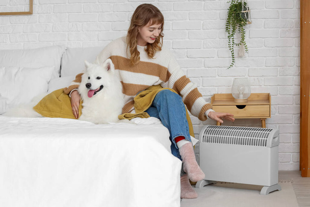 Jovem mulher com cobertor e Samoyed cão aquecendo perto do radiador no quarto - Foto, Imagem
