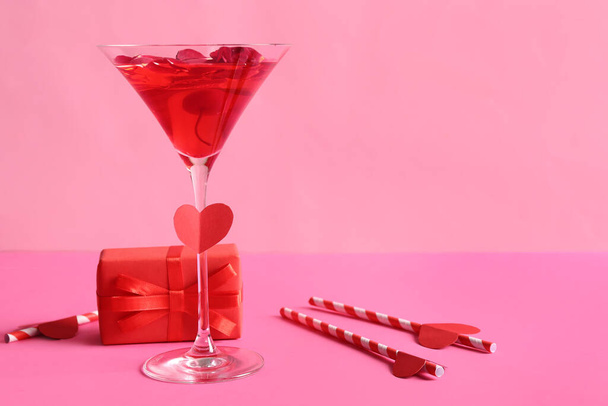 Copa de sabroso cóctel con pajitas y regalo sobre fondo rosa. Celebración de San Valentín - Foto, imagen