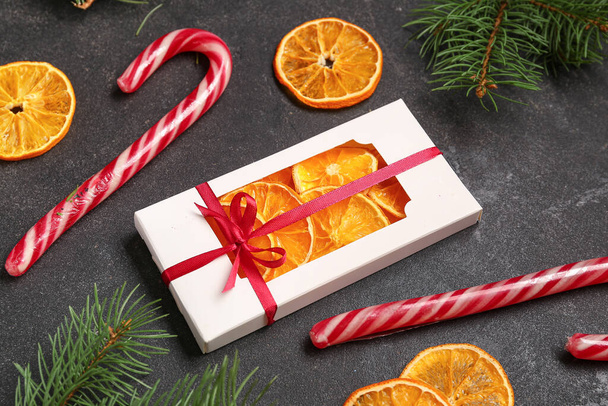 Scatola regalo con fette di arancia essiccate e bastoncini di zucchero natalizio su sfondo nero - Foto, immagini