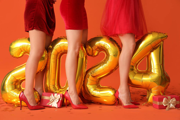 Junge Frauen mit Figur 2024 und Geschenken auf orangefarbenem Hintergrund. Neujahrsfeier - Foto, Bild