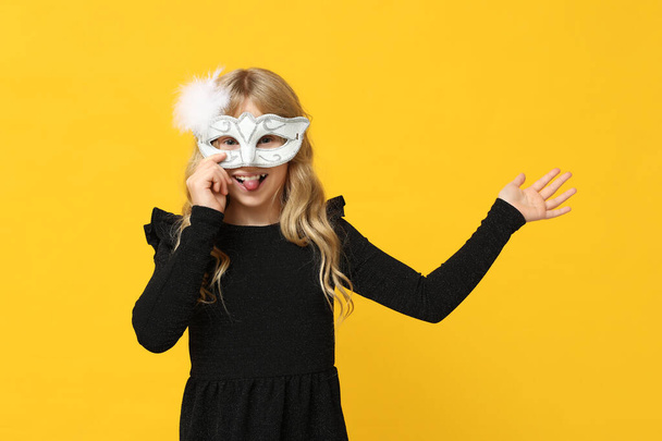 Roztomilé holčička nosí karneval masku a ukazuje něco na žlutém pozadí - Fotografie, Obrázek