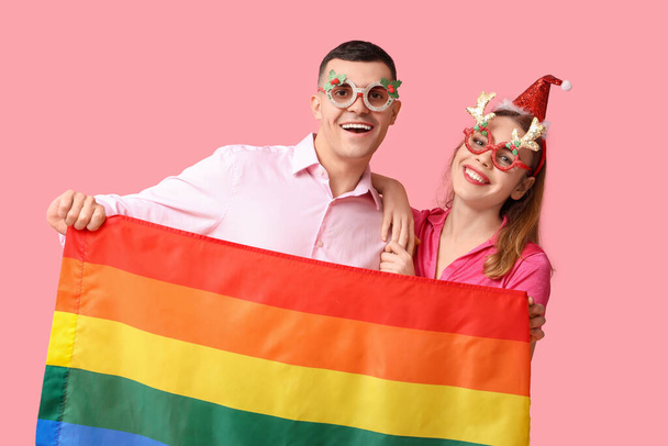 Jeune couple dans un décor de Noël avec drapeau LGBT sur fond rose - Photo, image