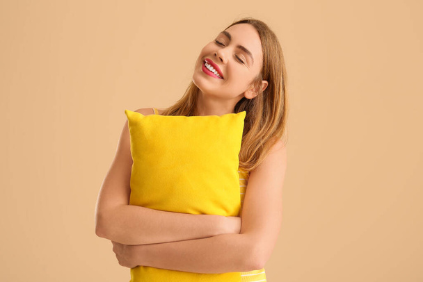 Mujer joven feliz con almohada suave amarilla sobre fondo beige - Foto, Imagen