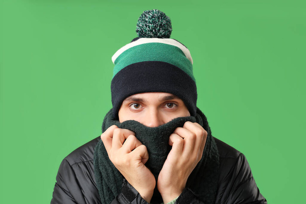 Young man in stylish puffer jacket and scarf on green background - Photo, Image