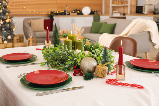 Праздничный стол с венком из омелы, горящими свечами и рождественскими украшениями - Фото, изображение