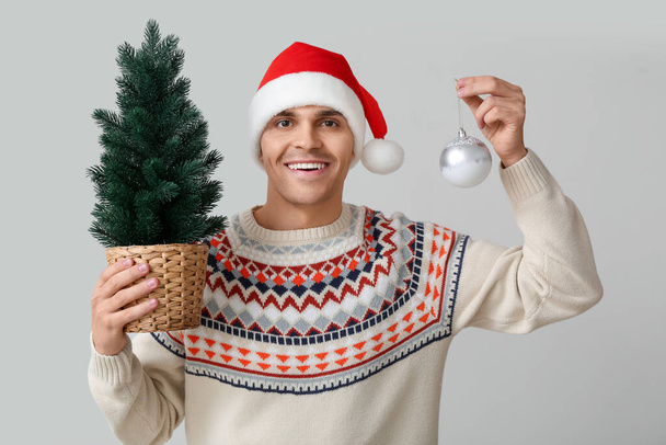 白い背景にクリスマスツリーとボールとサンタの帽子の若い男 - 写真・画像