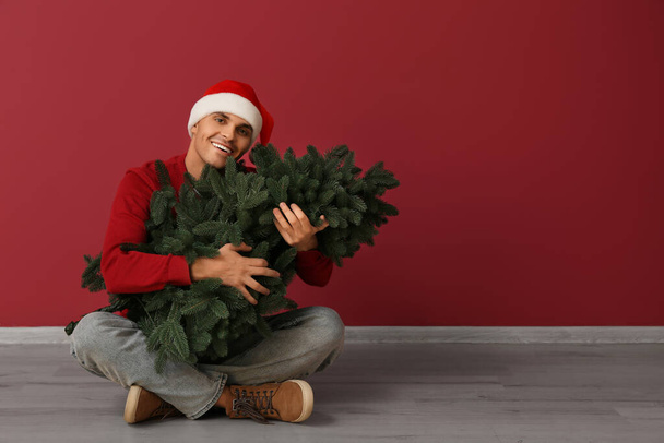 Young man in Santa hat with Christmas tree on red background - Photo, Image