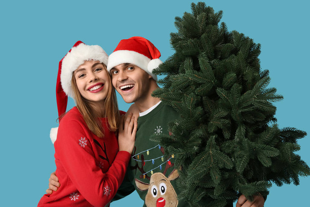 Glückliches junges Paar in Weihnachtsmützen mit Weihnachtsbaum auf blauem Hintergrund - Foto, Bild