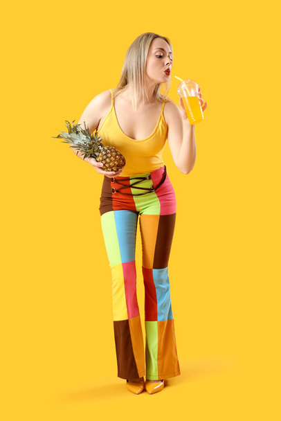 Bella giovane donna con succo di ananas bere su sfondo giallo - Foto, immagini