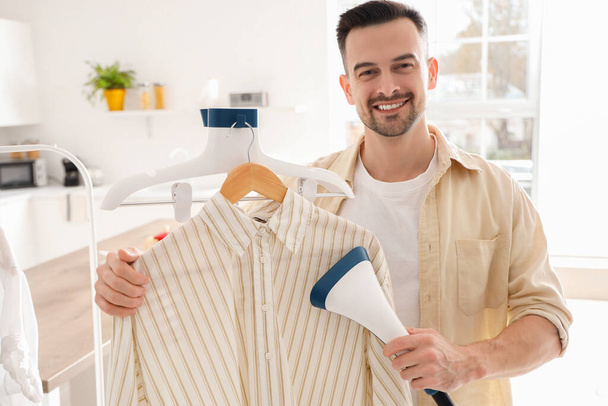Handsome man steaming shirt with modern steamer at home - Photo, Image