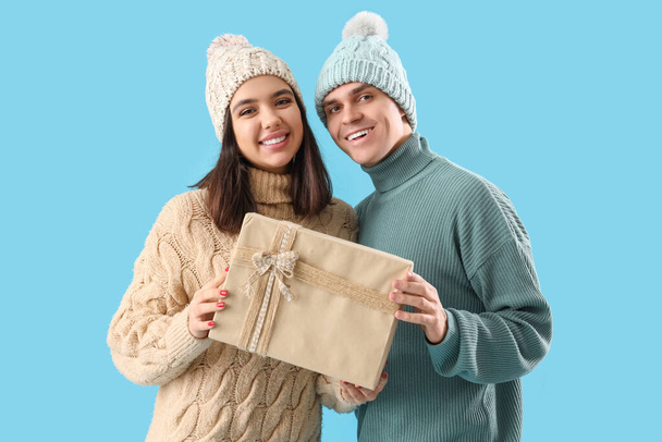 Happy young couple with Christmas gift on blue background - Photo, Image
