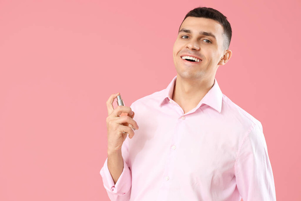 Jeune homme appliquant du parfum sur fond rose - Photo, image