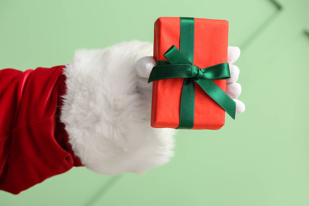 Санта рука з подарунковою коробкою на зеленій стіні, крупним планом - Фото, зображення