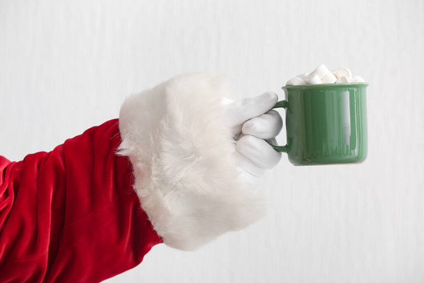 Santa Claus sosteniendo taza de sabrosa bebida de cacao con malvaviscos sobre fondo claro, primer plano - Foto, Imagen