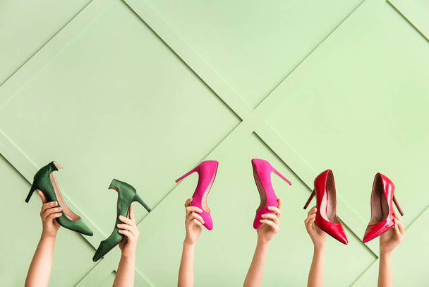 Female hands with stylish high heeled shoes against color wall - Photo, Image