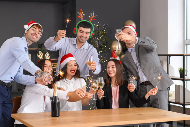 Jóvenes compañeros de trabajo con bengalas y champán celebrando el Año Nuevo en la fiesta corporativa en la oficina - Foto, Imagen