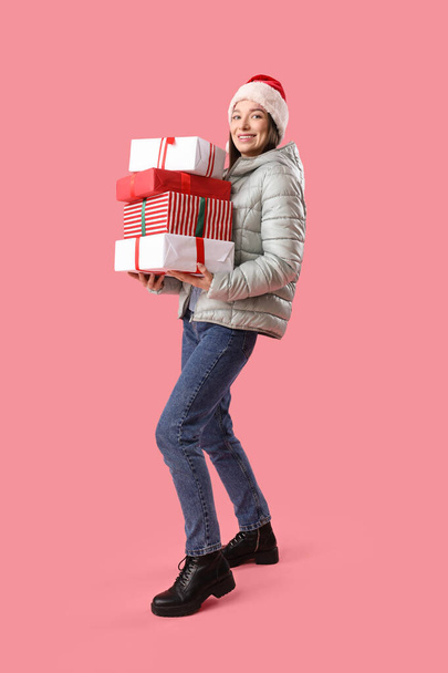Młoda kobieta w kapeluszu Santa z prezentów świątecznych na różowym tle - Zdjęcie, obraz
