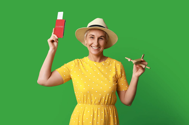 Mature female traveler with passport and wooden airplane on green background - Photo, Image
