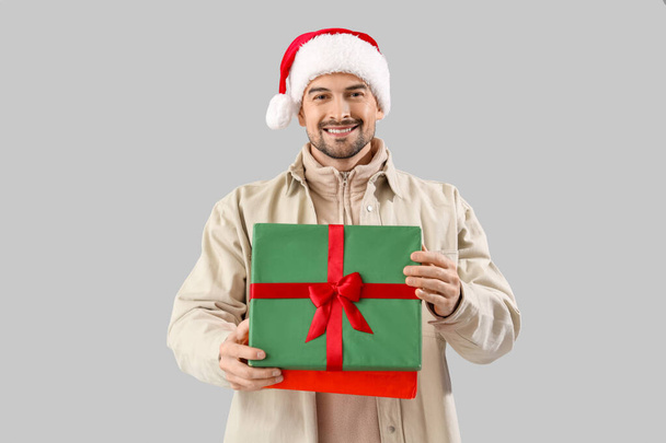 Schöner Mann mit Weihnachtsmütze mit Weihnachtsgeschenk auf hellem Hintergrund - Foto, Bild