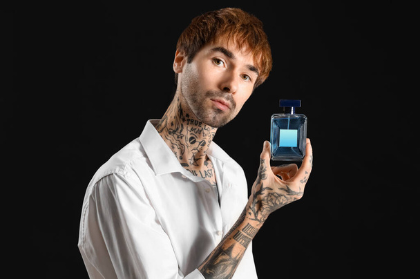 Tattooed young man with perfume on dark background - Photo, Image