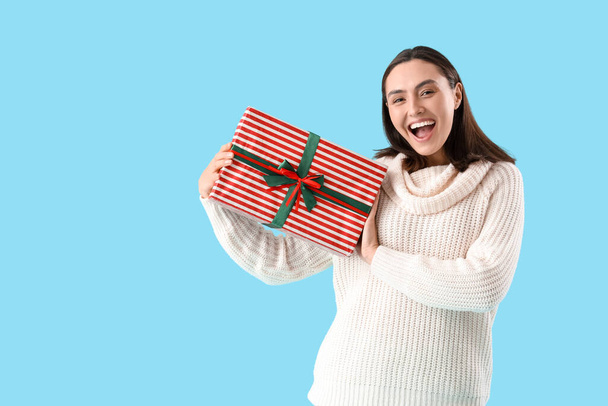 Happy young woman with Christmas present on blue background - Photo, Image