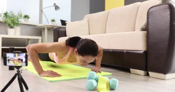 Jonge vrouw doet push-ups op tapijt thuis. Thuis oefening en kracht training concept - Video