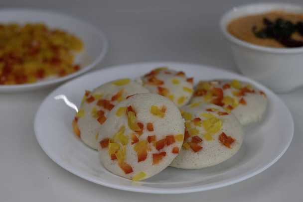 Pimiento salado servido ociosamente con chutney de coco. Un colorido y apetitoso desayuno del sur de la India. Pastel de arroz salado al vapor hecho con masa fermentada de lentejas y arroz cubierto con pimientos - Foto, Imagen