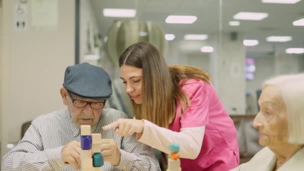 Wideo przyjaznej pielęgniarki pomaga starszemu mężczyźnie rozwiązać grę umiejętności, a następnie uśmiech - Materiał filmowy, wideo