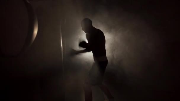 Male boxer impacting on punching bag over black smoke background. Boxer training hard. Copy space - Footage, Video