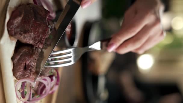 Close-up van vrouwelijke handen snijden een stuk varkensvlees kebab, vrouw die kebab diner in restaurant. Verticale video - Video