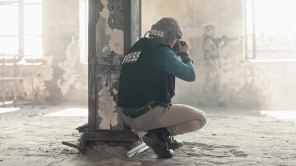 Πίσω όψη δημοσιογράφου που τραβάει φωτογραφίες στρατιωτικών που κρύβονται από βομβαρδισμούς σε εγκαταλελειμμένο κτίριο. Στρατιωτική αντίληψη. Άτομα που φορούν κράνη ασφαλείας και αλεξίσφαιρα γιλέκα κατά τη σύγκρουση - Πλάνα, βίντεο