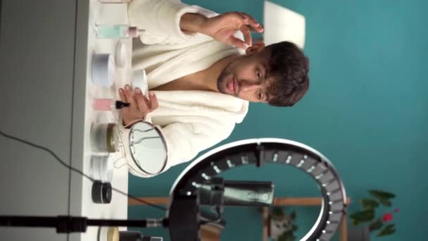 esteticista hacer tutorial de maquillaje en el teléfono inteligente en casa. El blogger árabe en albornoz aplica crema en la cara, grabando transmisión en vivo. Cuidado de la piel hidratante concepto de tratamiento de spa de belleza. Vertical - Metraje, vídeo